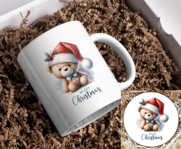 Weihnachtstasse mit niedlichem Teddybär-Motiv und passendem Untersetzer: Ein süßer Teddybär trägt eine rote Weihnachtsmütze mit Beeren und Stechpalmenblättern und eine kleine blaue Schleife um den Hals. Unter dem Motiv steht der Schriftzug ‚Merry Christma